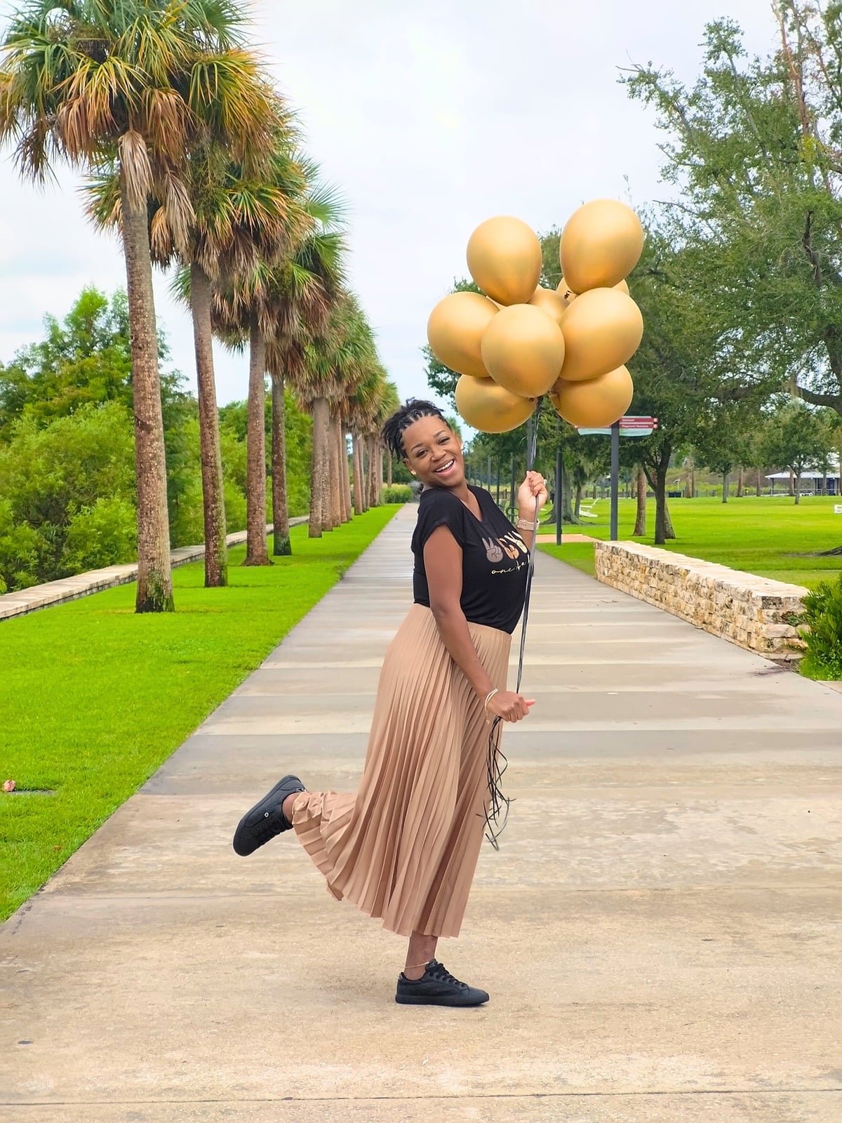 Charlene, founder of Created Crafty, holding a bouquet of gold balloons on a palm-lined walkway