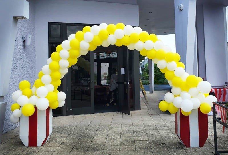 Yellow and white deluxe balloon arch over an entrance with striped bases