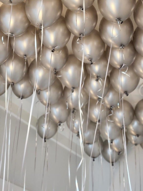 Ceiling filled with pearl silver helium balloons and trailing ribbons