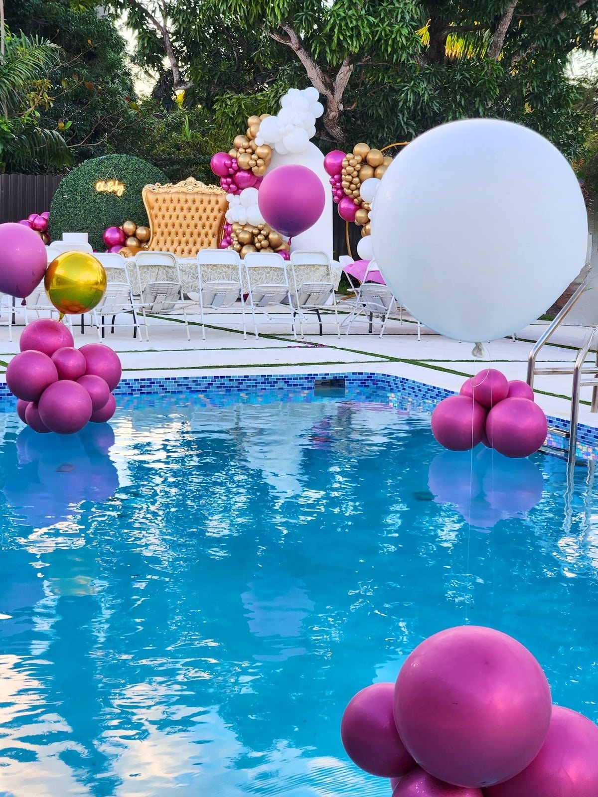 Poolside balloon installation in magenta, gold and white with a gold throne and greenery wall