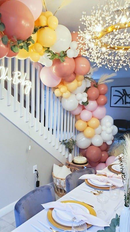 Neon sign beside a peach and cream balloon garland along a staircase