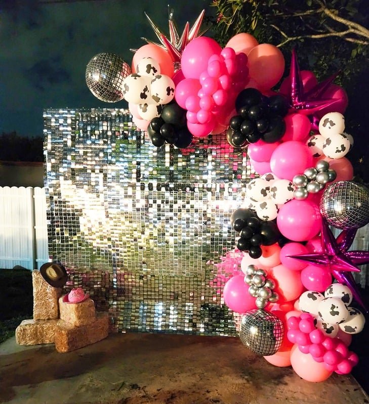 Silver shimmer sequin wall framed by hot pink balloons and disco balls